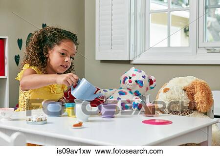 Girl in playroom sitting at table serving tea from toy tea set to soft toys View Large Photo Image Stock Photo - Girl in playroom sitting at table serving tea from toy tea set to soft toys. Fotosearch
