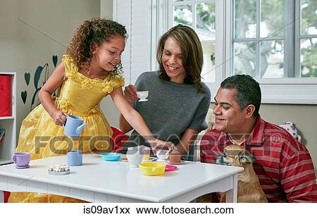 Girl in playroom sitting at table serving tea from toy tea set to parents View Large Photo Image Stock Photo - Girl in playroom sitting at table serving tea from toy tea set to parents. Fotosearch