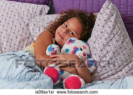 Stock Photography - Girl lying in bed cuddling teddy bear looking at camera. Fotosearch