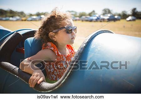 Stock Image - Girl sitting in barrel cart, wearing sunglasses looking away. Fotosearch