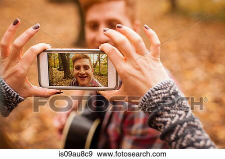 Stock Photo - Hands of young woman photographing boyfriend on smartphone in autumn forest. Fotosearch