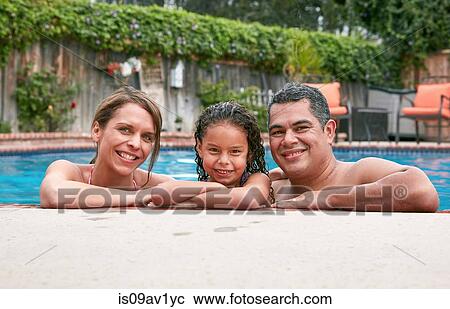 Stock Image - Head and shoulders of girl in swimming pool with parents looking at camera smiling. Fotosearch