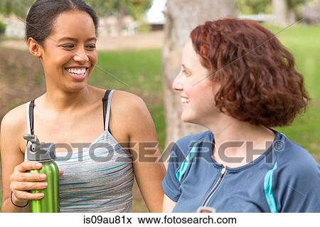 Head and shoulders of young women carrying water bottles face to face smiling View Large Photo Image Stock Photo - Head and shoulders of young women carrying water bottles face to face smiling. Fotosearch