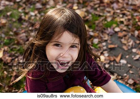 Stock Photograph - High angle portrait of young girl among autumn leaves looking at camera open mouthed smiling. Fotosearch