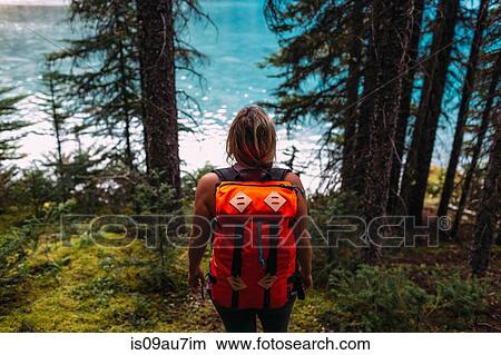 High angle rear view of mid adult woman carrying orange colour backpack standing in forest looking at water, Moraine lake, Banff National Park, Alberta Canada View Large Photo Image Picture - High angle rear view of mid adult woman carrying orange colour backpack standing in forest looking at water, Moraine lake, Banff National Park, Alberta Canada. Fotosearch