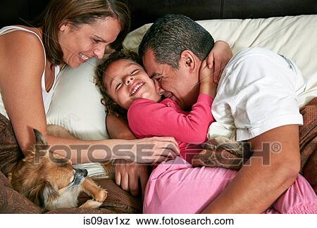Stock Photo - High angle view of girl in bed with parents and dog, hugging, tickling, smiling. Fotosearch