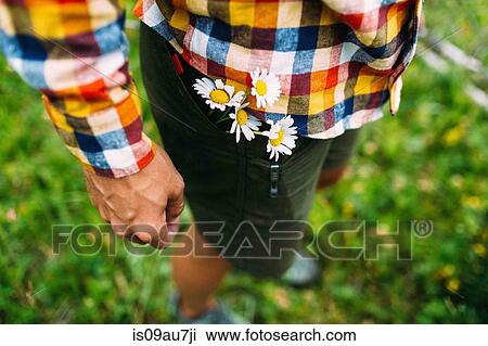 Stock Image - High angle view of mid adult man wearing checked shirt with daisies in shorts pocket, Moraine lake, Banff National Park, Alberta Canada. Fotosearch