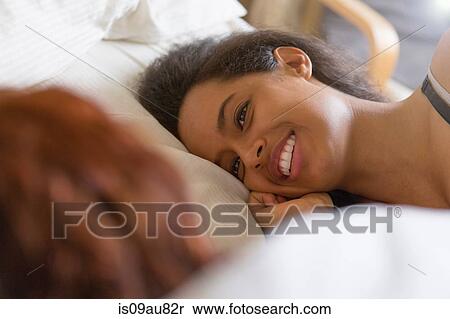 Stock Photography - Lesbian couple lying on side in bed face to face smiling. Fotosearch