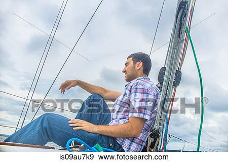 Stock Photo - Low angle side view of young man on sailboat looking away smiling. Fotosearch