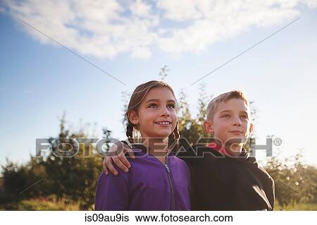 Low angle view of boy outdoors with arms around girl looking away smiling View Large Photo Image Stock Photograph - Low angle view of boy outdoors with arms around girl looking away smiling. Fotosearch