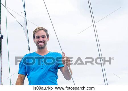Low angle view of young man holding onto sailboat ropes looking at camera smiling View Large Photo Image Stock Image - Low angle view of young man holding onto sailboat ropes looking at camera smiling. Fotosearch