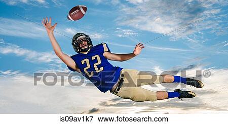 Male teenage American football player reaching to catch ball mid air against blue sky View Large Photo Image Stock Photo - Male teenage American football player reaching to catch ball mid air against blue sky. Fotosearch