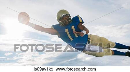 Male teenage American football player catching ball mid air against sunlit sky View Large Photo Image Stock Photography - Male teenage American football player catching ball mid air against sunlit sky. Fotosearch