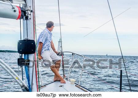 Mature man on bow of sailboat looking away towards lighthouse View Large Photo Image Stock Photography - Mature man on bow of sailboat looking away towards lighthouse. Fotosearch