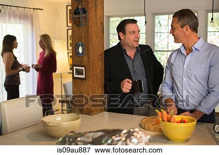Stock Photo - Mature men chatting whilst preparing food at dinner party. Fotosearch