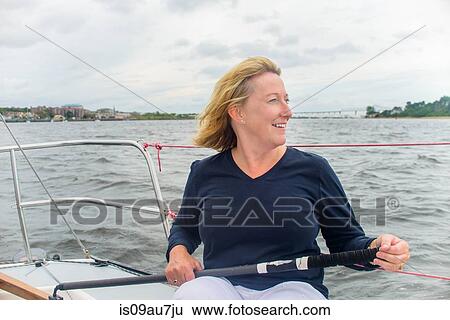 Stock Photograph - Mature woman streering sailboat looking away smiling. Fotosearch