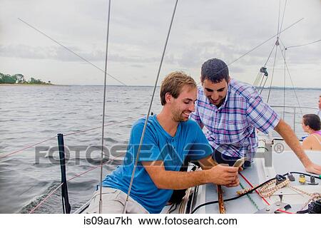 Men on sailboat looking at mobile phone smiling View Large Photo Image Stock Image - Men on sailboat looking at mobile phone smiling. Fotosearch