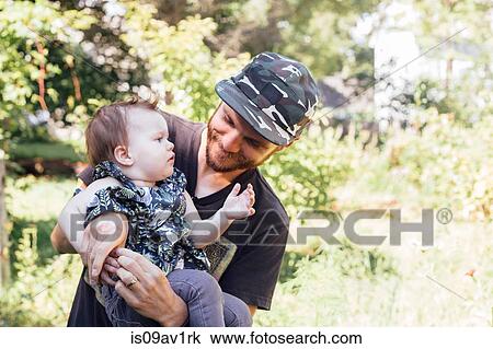 Stock Image - Mid adult man carrying baby daughter in woodland. Fotosearch