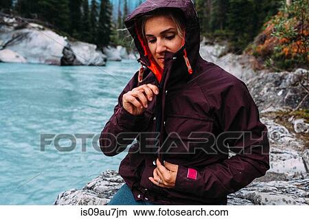 Picture - Mid adult woman by waters edge zipping up waterproof coat, Moraine lake, Banff National Park, Alberta Canada. Fotosearch