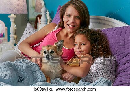 Mother and daughter and dog cuddling in bed looking at camera smiling View Large Photo Image Stock Photograph - Mother and daughter and dog cuddling in bed looking at camera smiling. Fotosearch