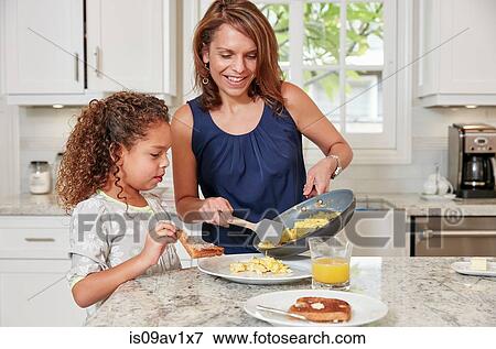 Stock Photo - Mother at kitchen counter serving daughter scrambled eggs from frying pan. Fotosearch