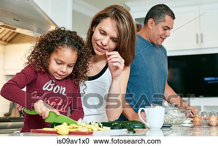 Stock Image - Mother helping daughter chop vegetables in kitchen. Fotosearch