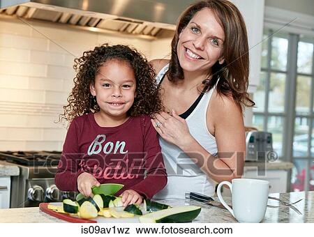 Mother helping daughter chop vegetables in kitchen, looking at camera smiling View Large Photo Image Stock Photo - Mother helping daughter chop vegetables in kitchen, looking at camera smiling. Fotosearch