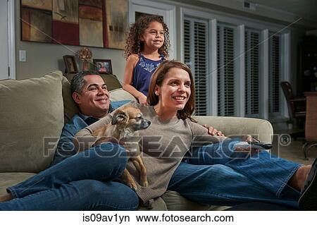 Parents and girl in living room on sofa with dog looking away smiling View Large Photo Image Picture - Parents and girl in living room on sofa with dog looking away smiling. Fotosearch