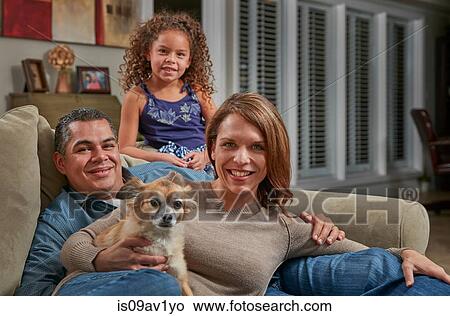 Parents and girl in living room on sofa with dog looking at camera smiling View Large Photo Image Picture - Parents and girl in living room on sofa with dog looking at camera smiling. Fotosearch