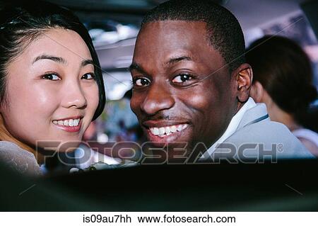 Stock Image - Portrait of couple looking over shoulder at camera smiling. Fotosearch
