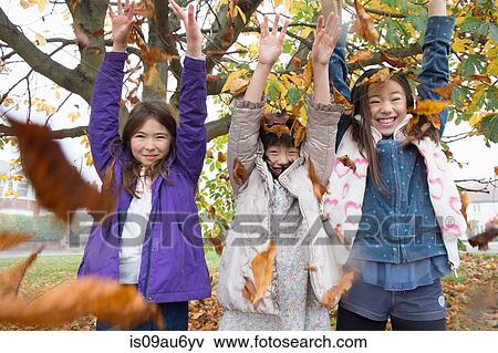 Stock Photo - Portrait of three young girls throwing autumn leaves. Fotosearch