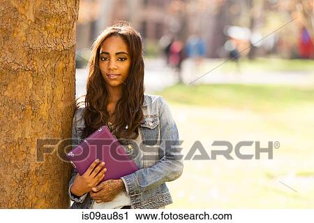 Portrait of young woman leaning against tree holding digital tablet looking at camera smiling View Large Photo Image Stock Image - Portrait of young woman leaning against tree holding digital tablet looking at camera smiling. Fotosearch