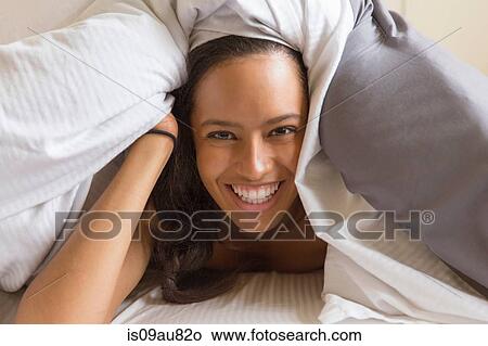 Picture - Portrait of young woman underneath quilt looking at camera smiling. Fotosearch