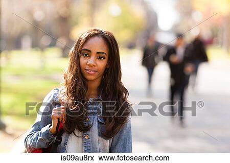 Stock Photo - Portrait of young woman with long brown hair wearing denim jacket looking at camera smiling. Fotosearch