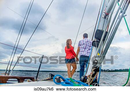 Rear view of couple on bow of boat holding hands, looking over shoulder at camera smiling View Large Photo Image Stock Photograph - Rear view of couple on bow of boat holding hands, looking over shoulder at camera smiling. Fotosearch