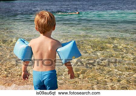 Rear view of cute boy wearing blue armbands paddling in sea View Large Photo Image Stock Photograph - Rear view of cute boy wearing blue armbands paddling in sea. Fotosearch