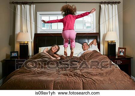 Stock Image - Rear view of girl in mid air jumping on parents bed. Fotosearch