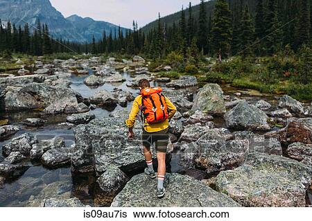 Rear view of mid adult man carrying backpack walking on rocky riverbed, Moraine lake, Banff National Park, Alberta Canada View Large Photo Image Stock Photograph - Rear view of mid adult man carrying backpack walking on rocky riverbed, Moraine lake, Banff National Park, Alberta Canada. Fotosearch