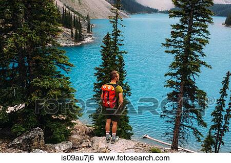 Rear view of mid adult man standing on cliff edge looking at elevated view of Moraine lake, Banff National Park, Alberta Canada View Large Photo Image Stock Photograph - Rear view of mid adult man standing on cliff edge looking at elevated view of Moraine lake, Banff National Park, Alberta Canada. Fotosearch
