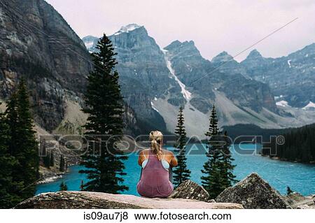 Stock Photo - Rear view of mid adult woman on cliff edge looking at alevated view of Moraine lake, Banff National Park, Alberta Canada. Fotosearch