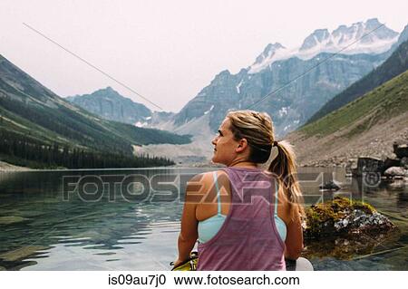 Rear view of mid adult woman sitting at waters edge looking away, Moraine Lake, Banff National Park, Alberta Canada View Large Photo Image Stock Image - Rear view of mid adult woman sitting at waters edge looking away, Moraine Lake, Banff National Park, Alberta Canada. Fotosearch