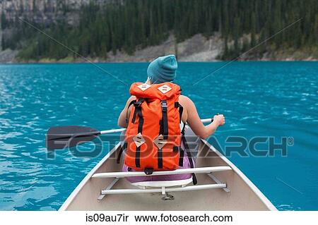 Stock Photography - Rear view of mid adult woman with orange colour backpack paddling canoe, Moraine lake, Banff National Park, Alberta Canada. Fotosearch
