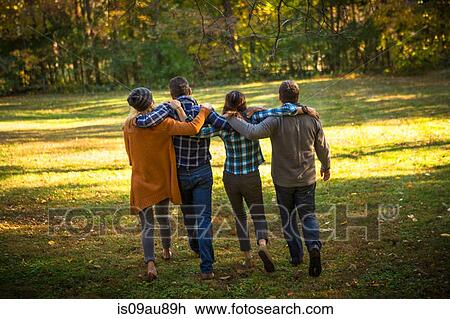 Stock Image - Rear view of two mature couples strolling in garden with arms around each other. Fotosearch