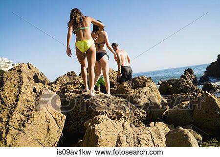 Stock Photo - Rear view of young adult friends exploring rocks on Newport Beach, California, USA. Fotosearch
