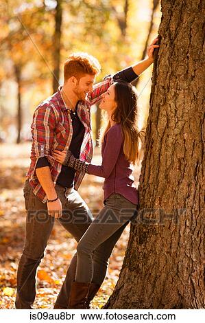 Stock Photography - Romantic young couple leaning against tree in autumn forest. Fotosearch