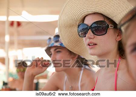 Row of teenage girls wearing sunhats relaxing under beach umbrellas View Large Photo Image Stock Image - Row of teenage girls wearing sunhats relaxing under beach umbrellas. Fotosearch