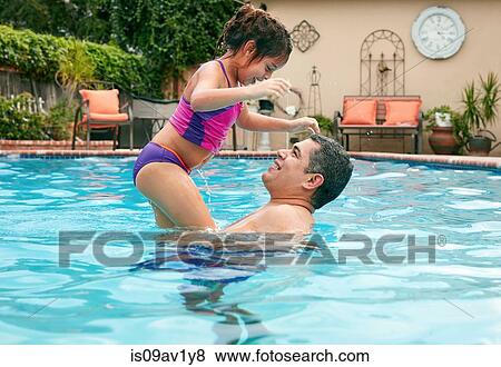Side view of father lifting up girl in swimming pool, face to face smiling View Large Photo Image Stock Photo - Side view of father lifting up girl in swimming pool, face to face smiling. Fotosearch