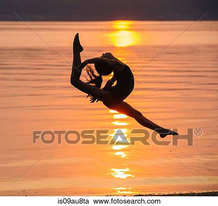Side view of girl in silhouette by ocean at sunset in mid air, legs apart throwing head back View Large Photo Image Stock Image - Side view of girl in silhouette by ocean at sunset in mid air, legs apart throwing head back. Fotosearch