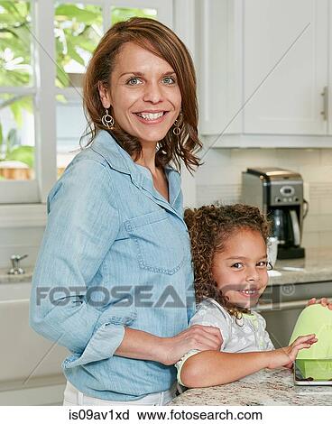 Side view of mother behind daughter in kitchen looking at camera smiling View Large Photo Image Stock Image - Side view of mother behind daughter in kitchen looking at camera smiling. Fotosearch