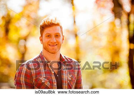 Stock Image - Sunlit portrait of red haired young man in forest. Fotosearch